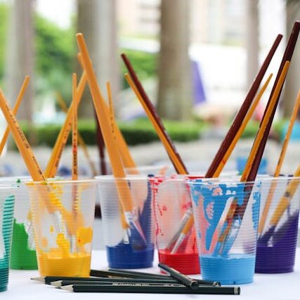 several plastic cups with colorful paint colors and brushes inside them