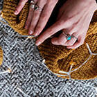 image of a person's hands knitting with brown yarn