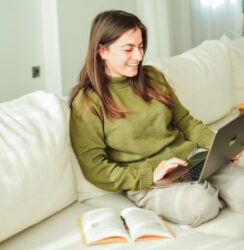 a smiling woman is in the couch reading from her laptop