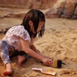 toddler in sand with a scoop and brush