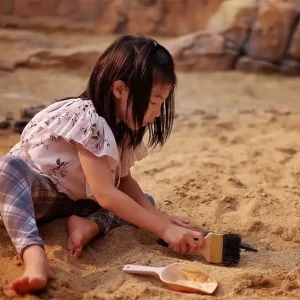 toddler in sand with a scoop and brush