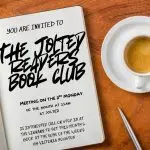 an open page of a book says "You are invited to The Jolted Readers Book Club. Meeting on the 3rd Monday of the month at 11AM." There is a cup of cappuchino and a pen next to the book