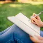 someone sitting in the grass drawing or writing in a journal