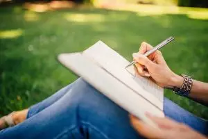 someone sitting in the grass drawing or writing in a journal