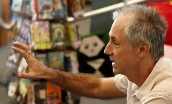 Stuart in the library, talking with his arm reached out